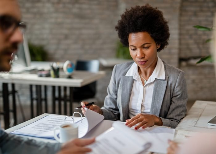 Black female financial advisor going through business reports while having a meeting with clients in the office.