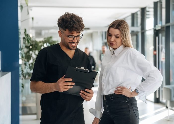 Showing information in notepad. Man and woman are indoors in modern building.