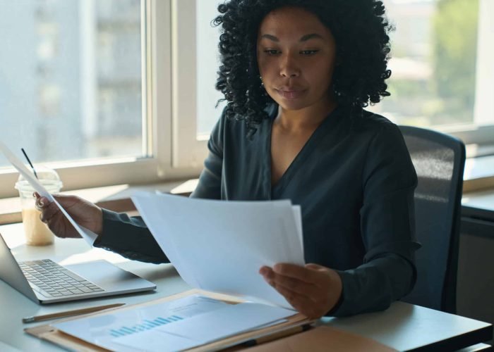 Multiracial female office manager is sitting at the table and looking through working documents